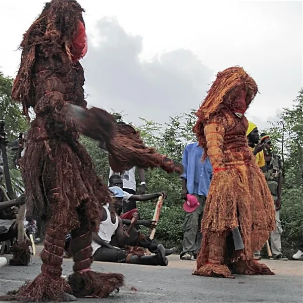 Deux Kankourangs, personnages masqués recouverts de fibres d'écorce rouge, dans une rue de Ziguinchor