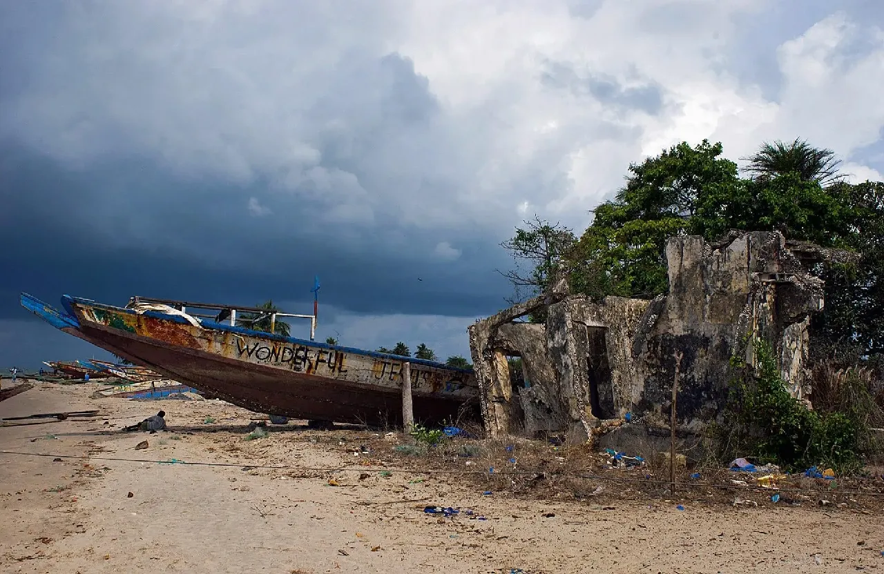 La plage de Diogué : la pirogue « Wonderful Jesus » échouée près d'un bâtiment en ruine, sous un ciel d'orage