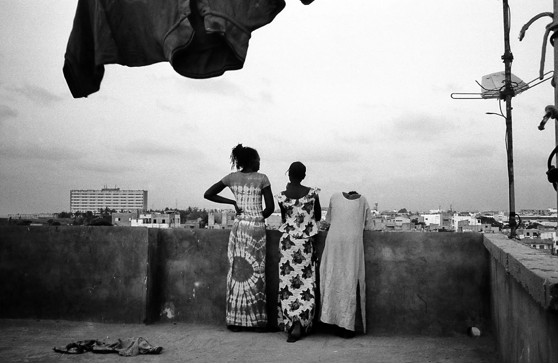 Trois femmes et une robe suspendue sur un toit-terrasse face à la ville, en noir et blanc
