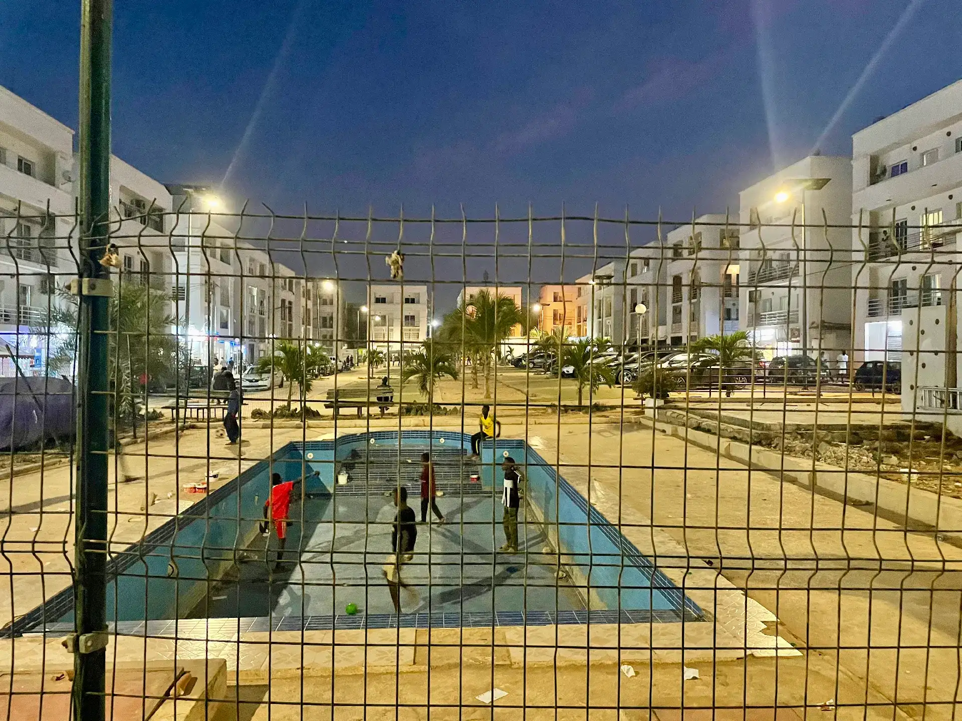 Piscine à sec derrière un grillage dans une résidence bétonnée, à la tombée de la nuit