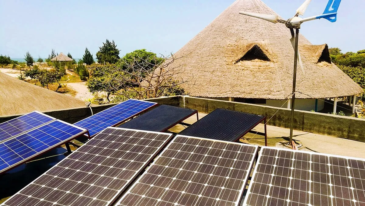 Panneaux solaires et éolienne devant un toit de chaume du Papayer Écolodge