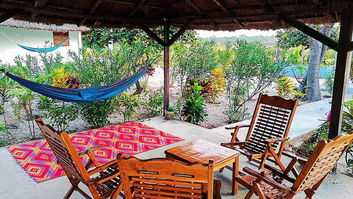 Patio ombragé avec hamac et fauteuils en bois face au jardin tropical